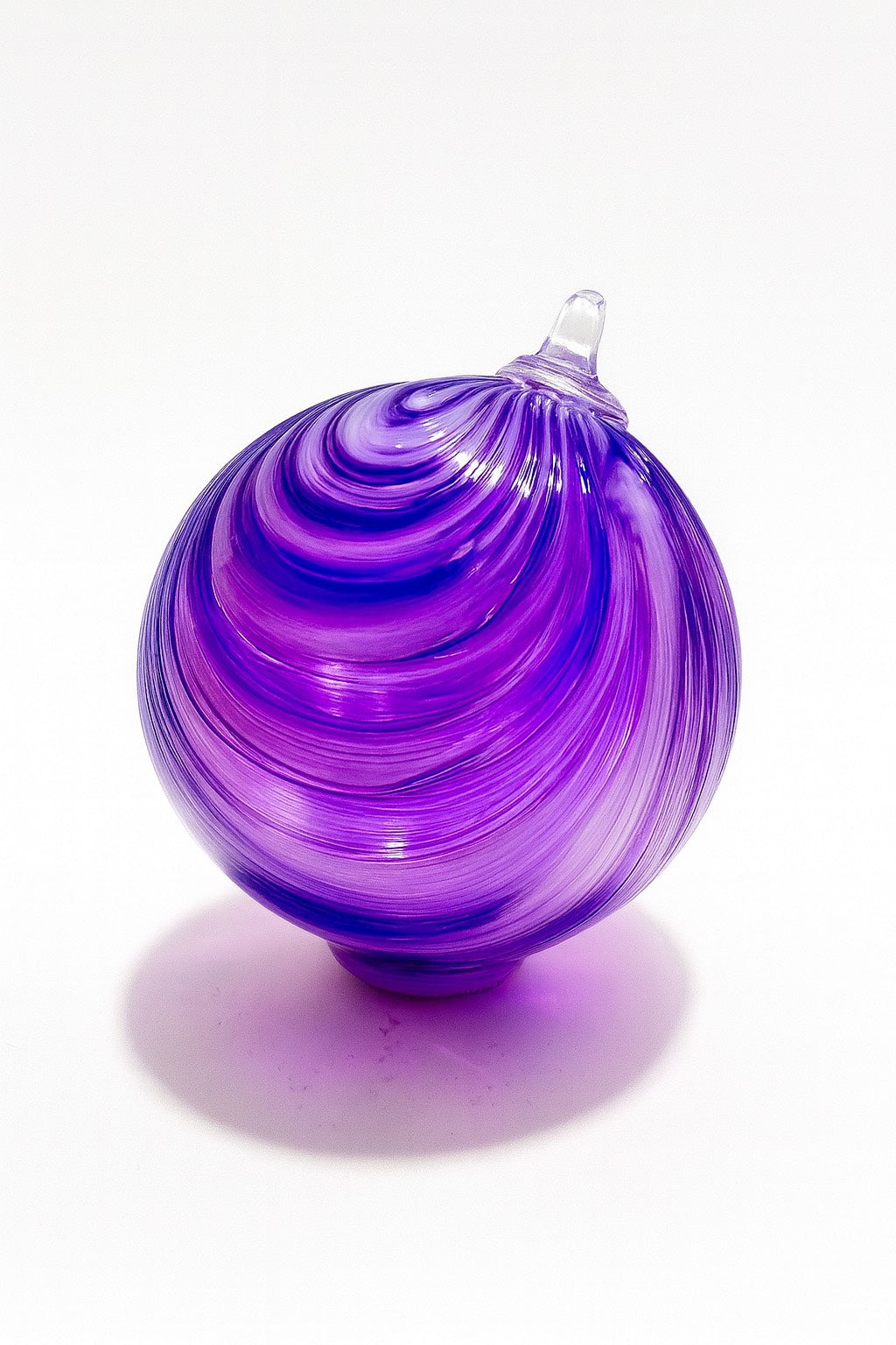 Hand-blown purple glass ornament with swirl design from Puget Sound Glassblowing Studio on a white background.